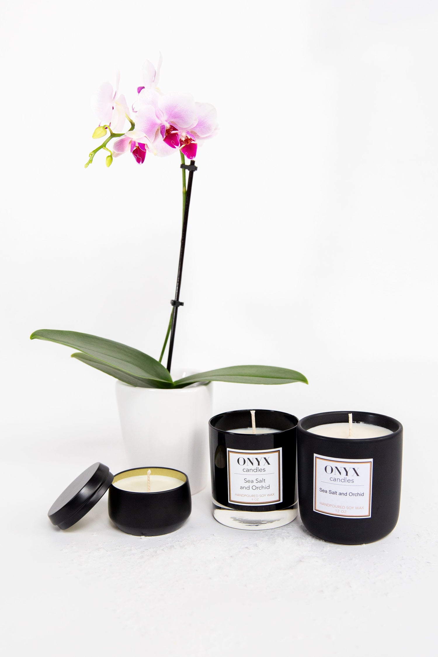 Three size variants for the Onyx candle scent Sea Sald and Orchid, shown with a pink Orchid blooming behind the candles