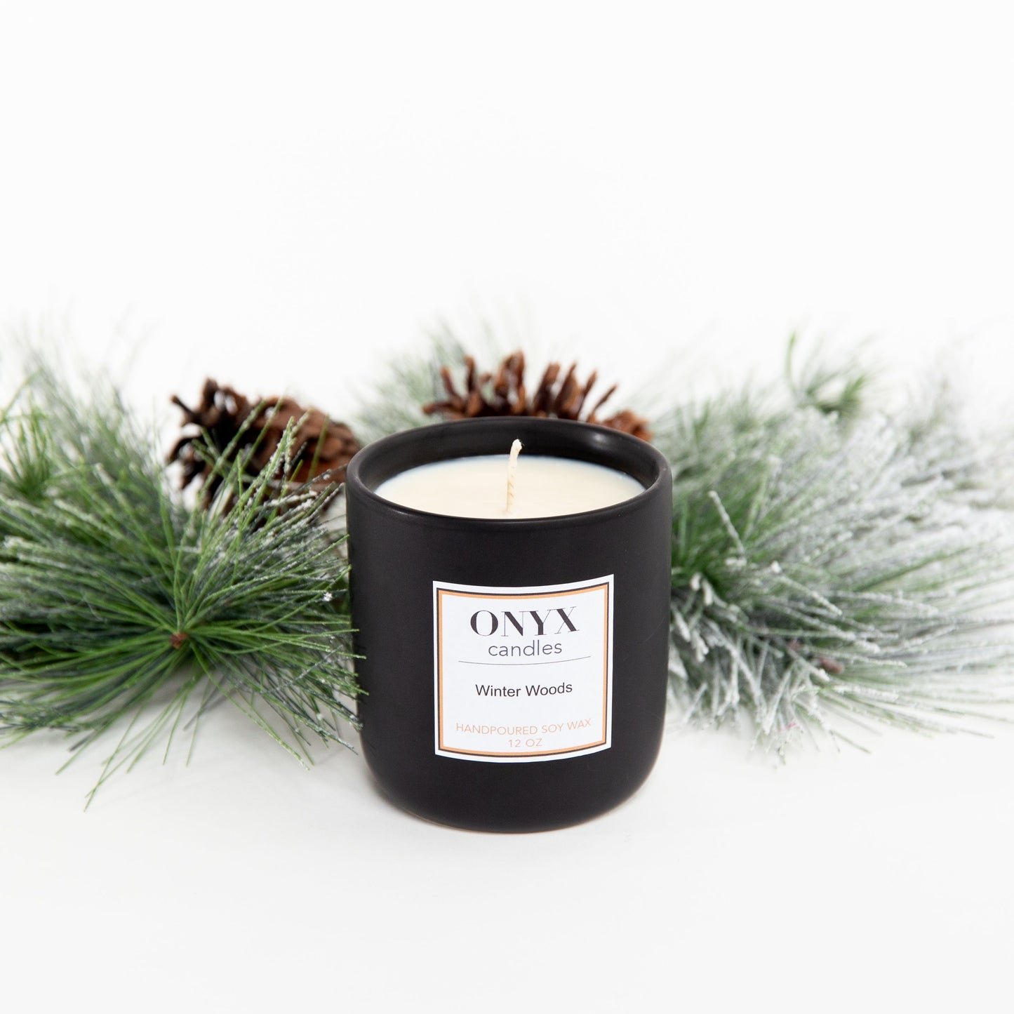 Winter Woods candle in a 12 oz matte black ceramic jar, the candle sits upon winter greens and pinecones