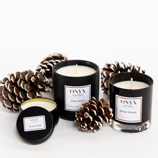 pictured left to right is the 4 oz matte black tin, the 12 oz matte black ceramic jar, and the 9 oz black glass jar variants of Onyx candles in the scent Winter Woods. Candles are sitting on a white background with snow covered pinecones